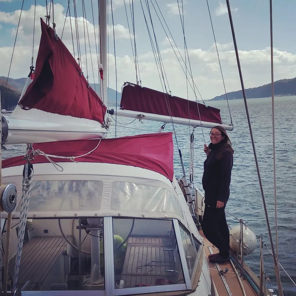 Proud woman standing on a sailboat for anchor showing off her DIY sail bags and bimini.  