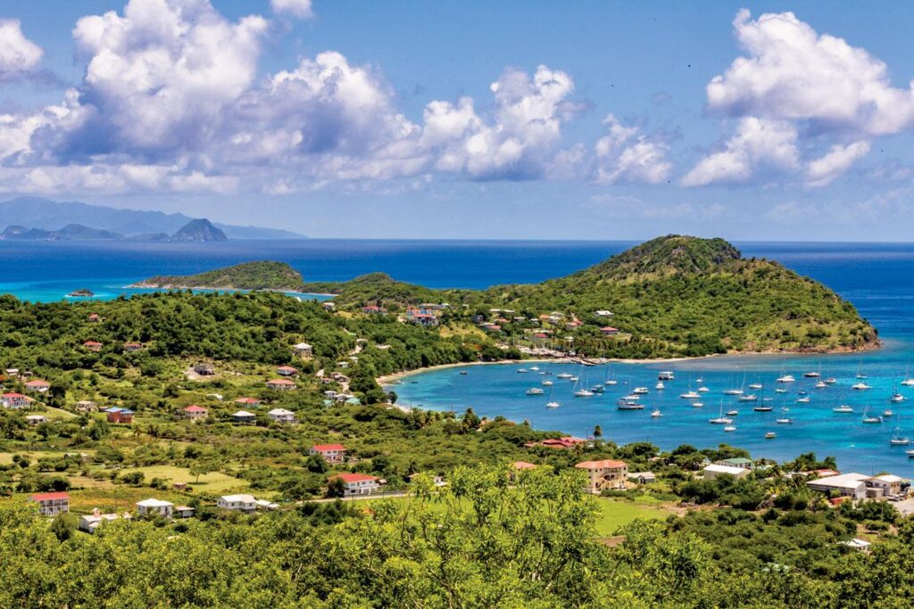 Tyrell Bay in Carriacou with anchored sailboats, turquoise water and lush green Caribbean hills.
